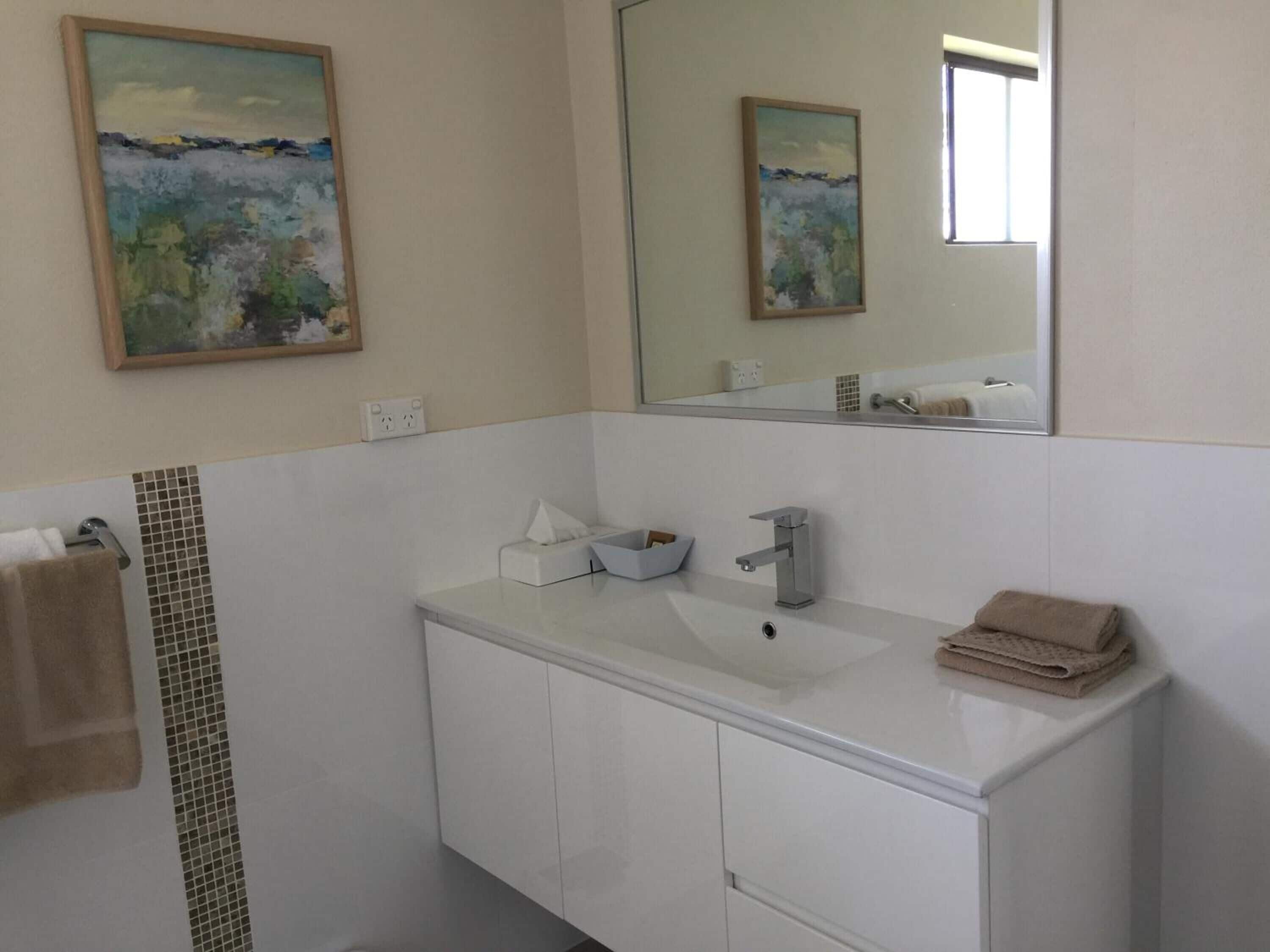A bathroom with a white sink, a mirror, and a painting on the wall.