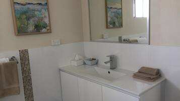 A bathroom with a white sink, a mirror, and a painting on the wall.