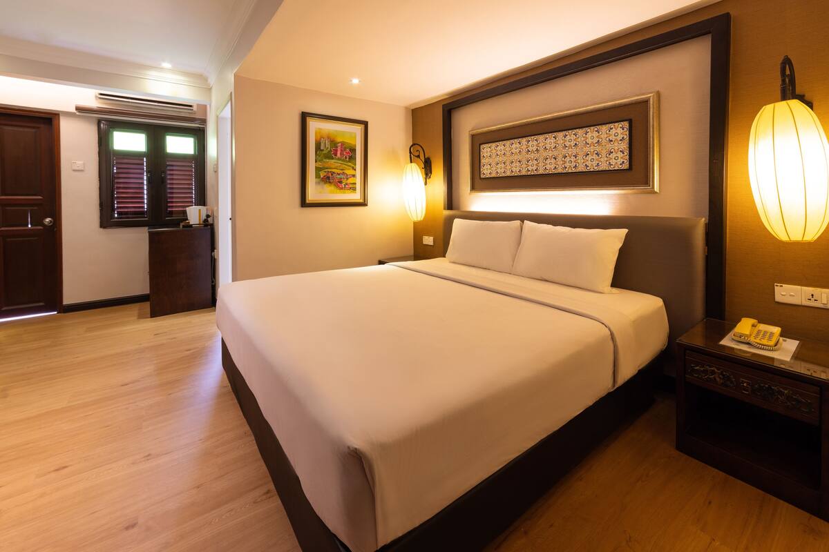 A hotel room with a large bed, a bedside table with a lamp, and a wall-mounted telephone.
