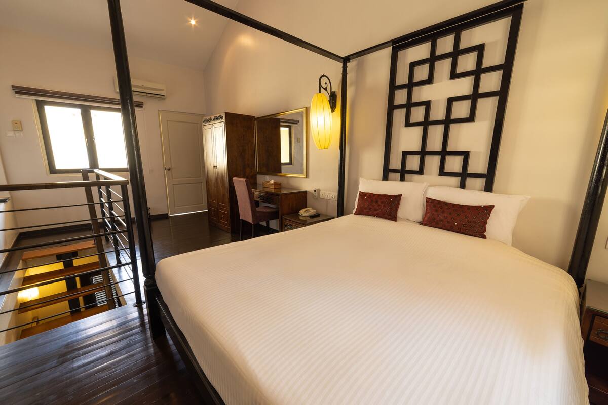 A hotel room with a large bed, a desk with a chair, a mirror, and a staircase.