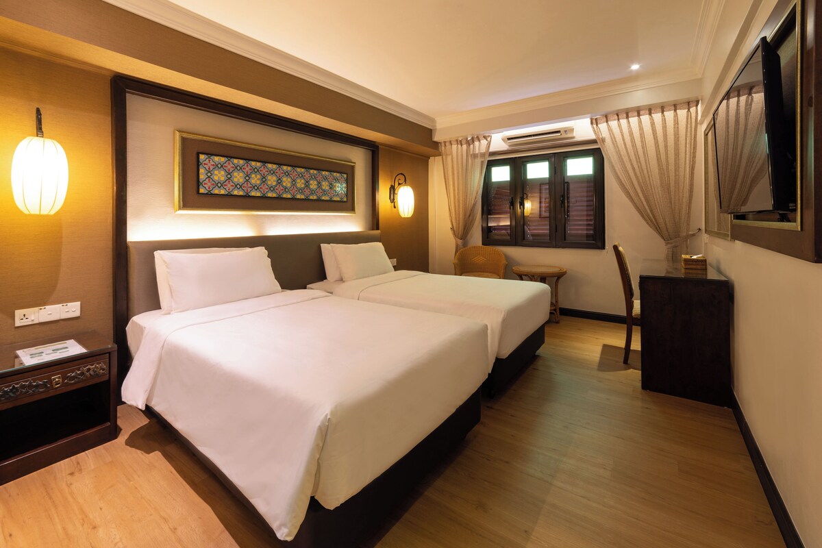A hotel room with two beds, a desk, a chair, a TV, and a window with curtains.