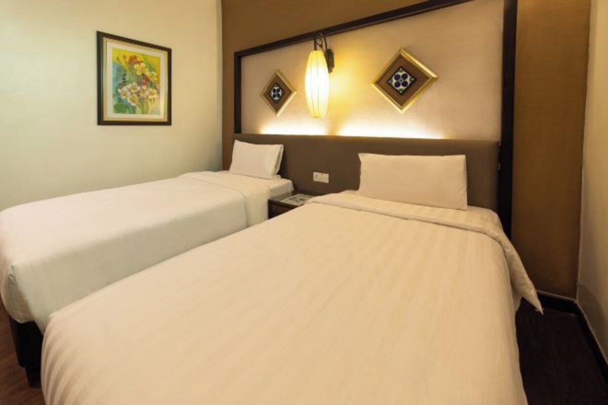 A hotel room with two beds, a nightstand, a lamp, and a framed picture on the wall.