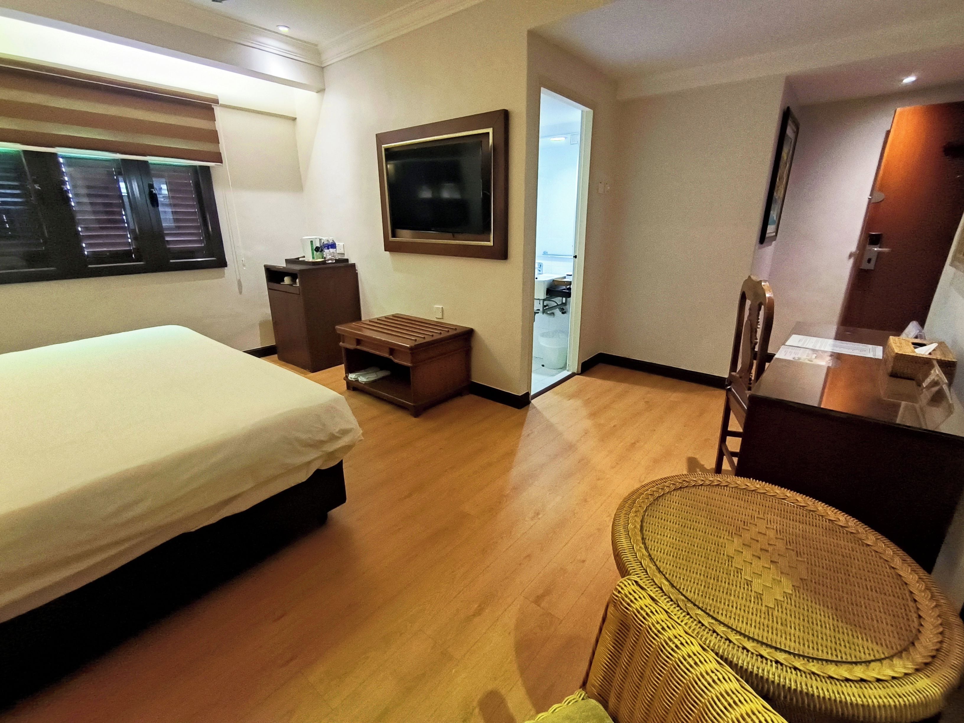 Een hotelkamer met een bed, een bureau, een stoel, een klein tafeltje en een raam met zonwering.