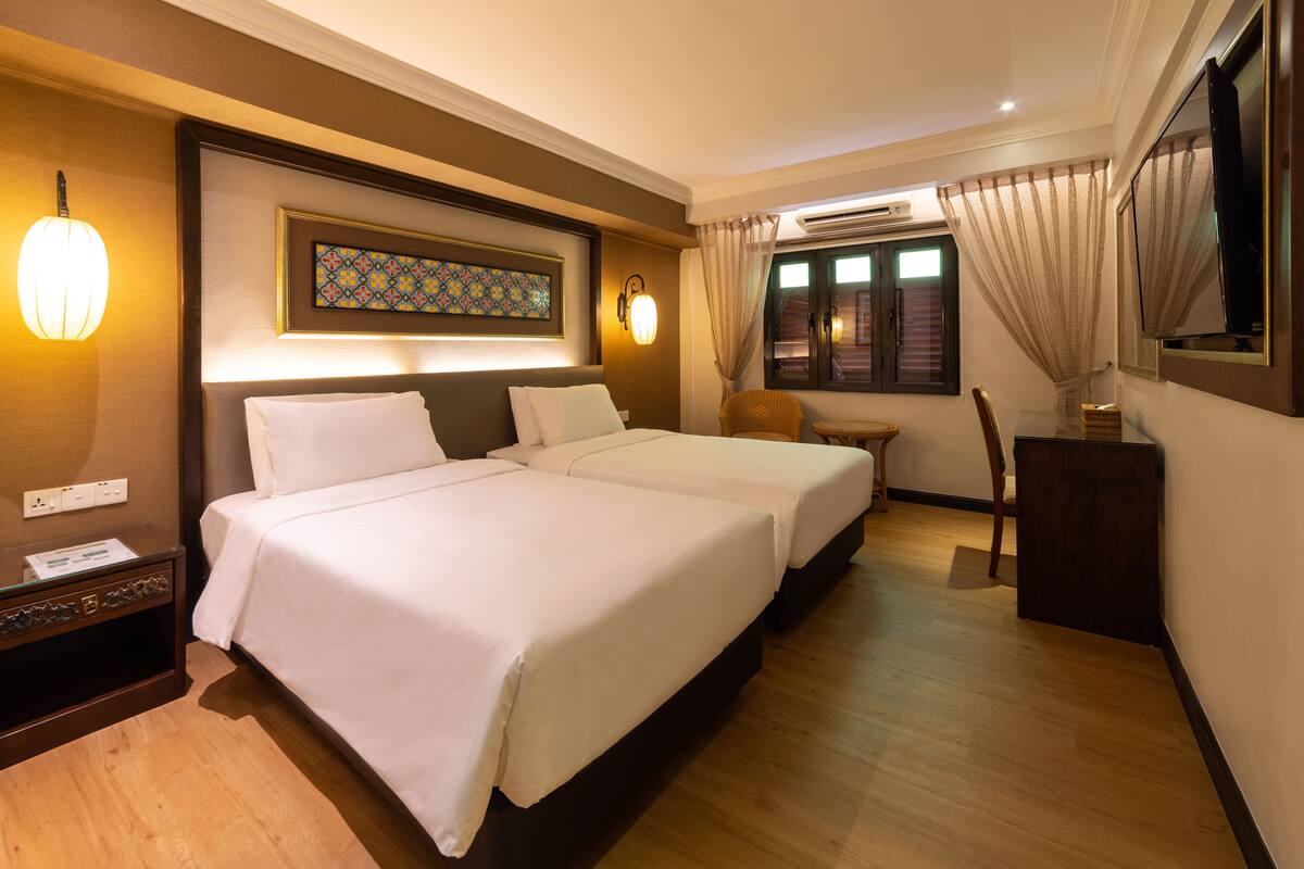 A hotel room with two beds, a desk, a chair, a TV, and a window with curtains.