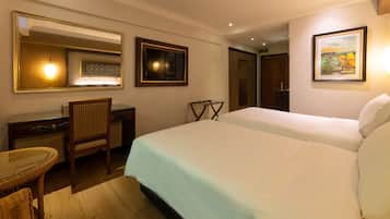 Quarto de hotel com cama, escrivaninha, cadeira, espelho e um quadro na parede.