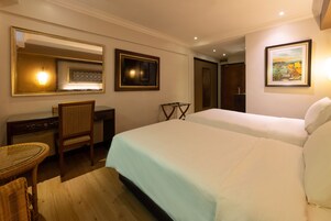 Quarto de hotel com cama, escrivaninha, cadeira, espelho e um quadro na parede.