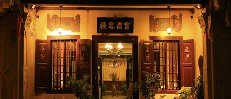 A traditional building entrance with a sign, wooden doors, and potted plants.