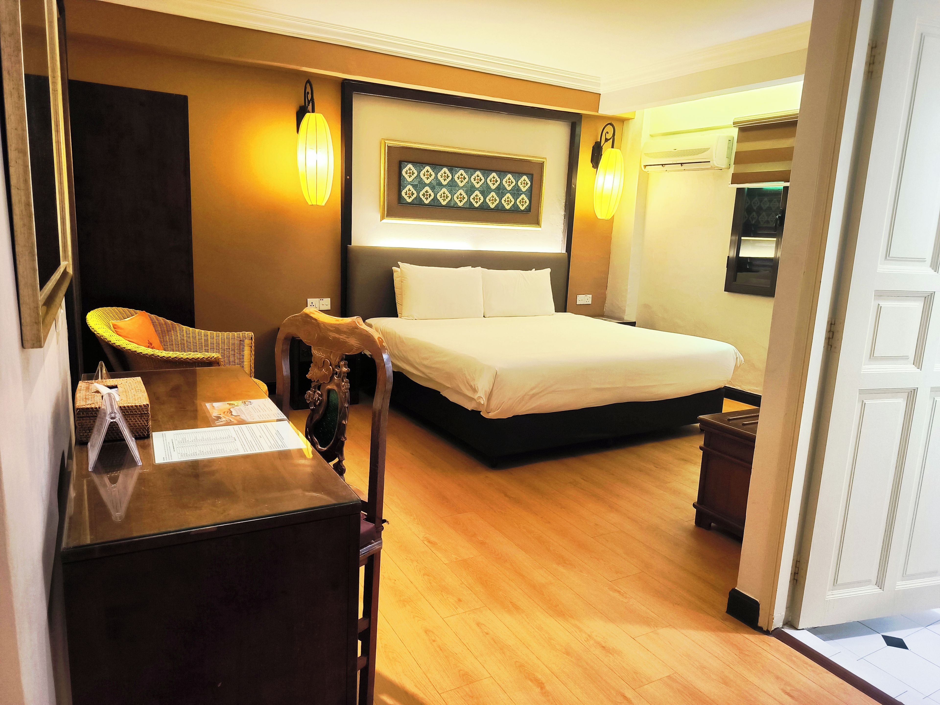 A hotel room with a bed, bedside tables, a lamp, a wall-mounted artwork, and a wooden floor.
