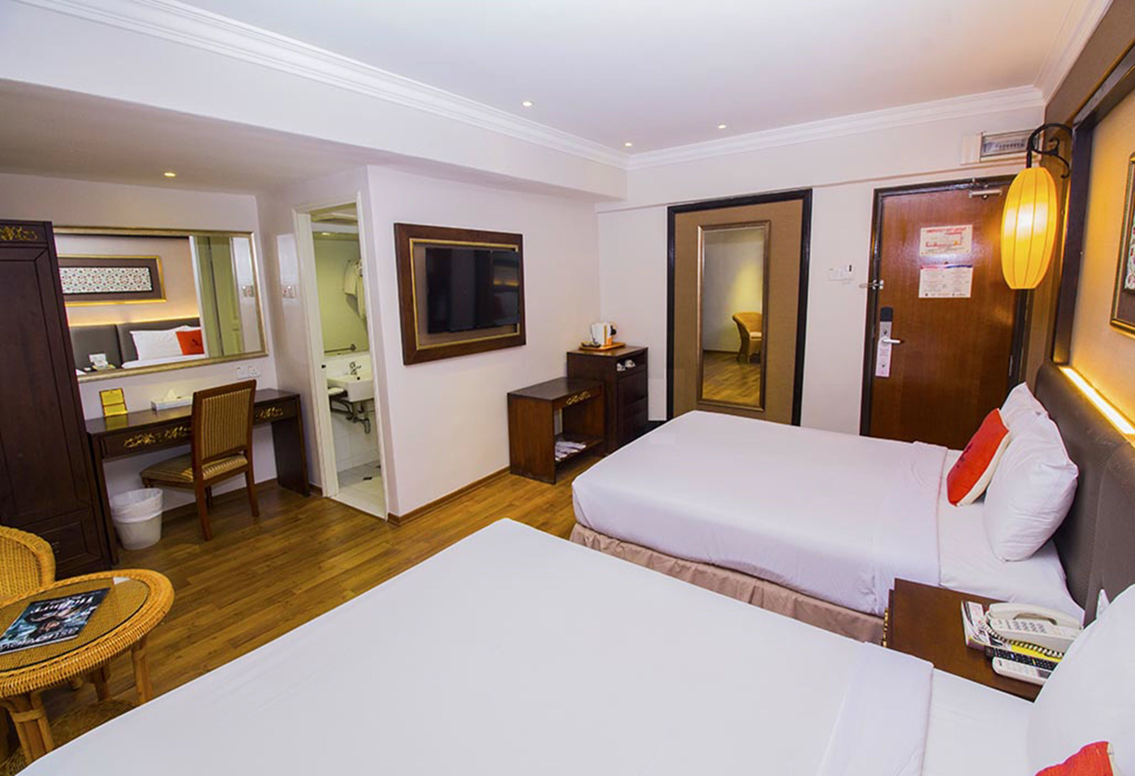 A hotel room with two beds, a desk, a chair, a television, and a bathroom visible through an open door.