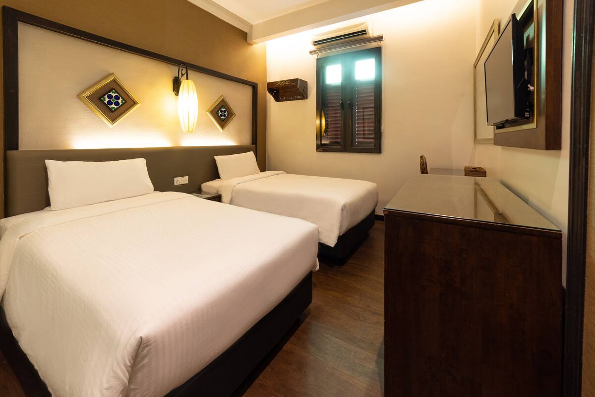 A hotel room with two beds, a nightstand, a mirror, and a wall-mounted air conditioning unit.