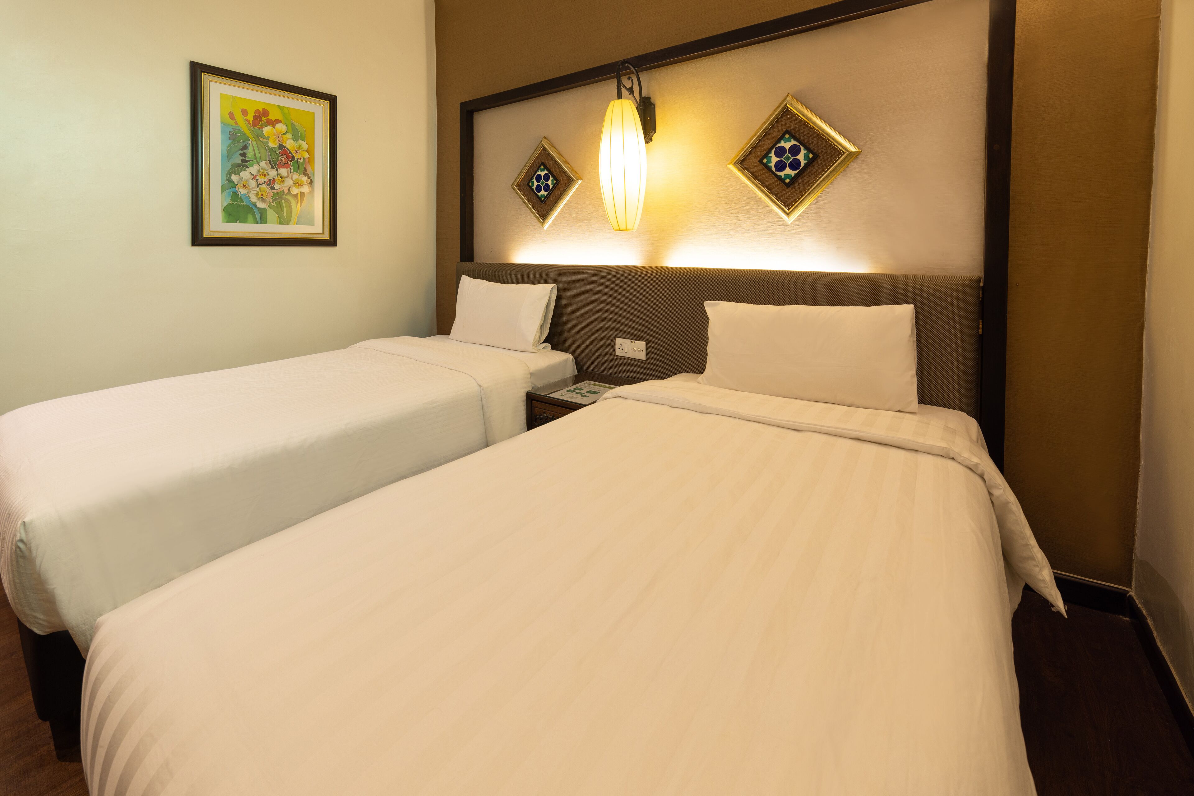 A hotel room with two single beds, a nightstand, a telephone, and a wall-mounted light fixture.