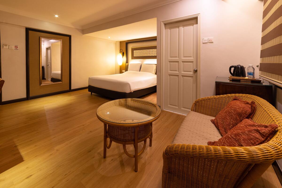 A hotel room with a bed, a glass-top table, a wicker sofa, and a door leading to another room.
