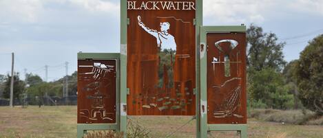 A metal sign with the text "BLACKWATER" and illustrations of a person taking a photo, a fish, and a diver.