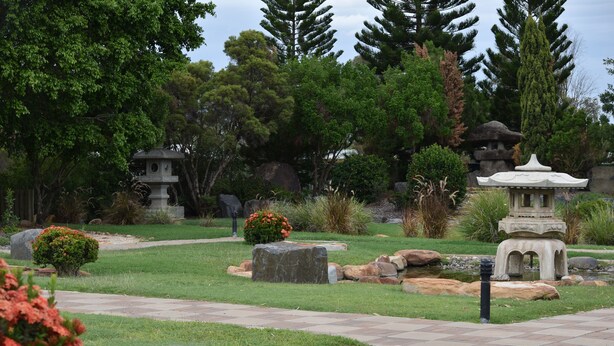 A garden with stone statues, a pond, and various plants. - Black Diamond Motel (Blackwater)