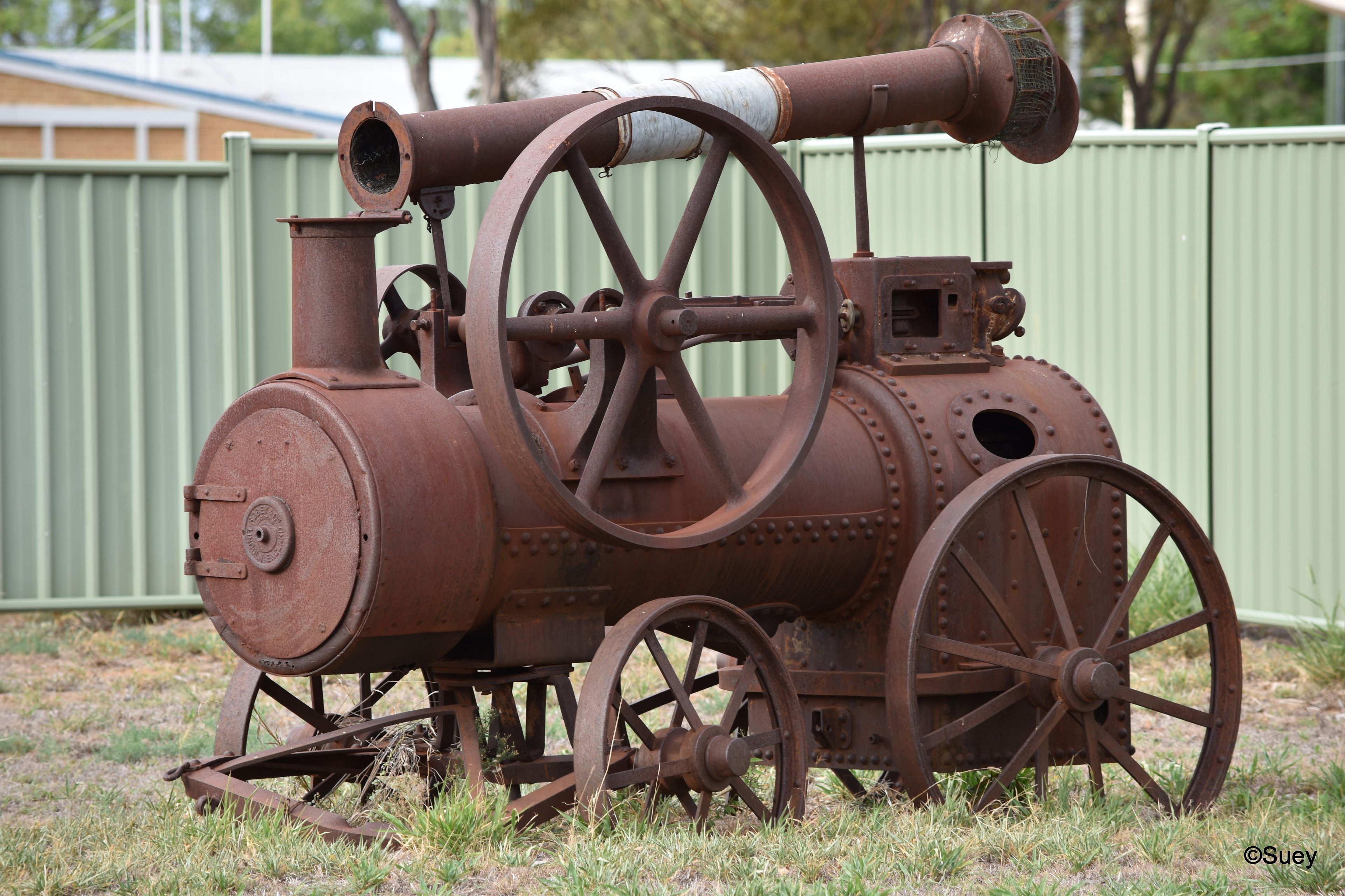 An old, rusted steam engine with large wheels and a chimney, placed outdoors on grass.