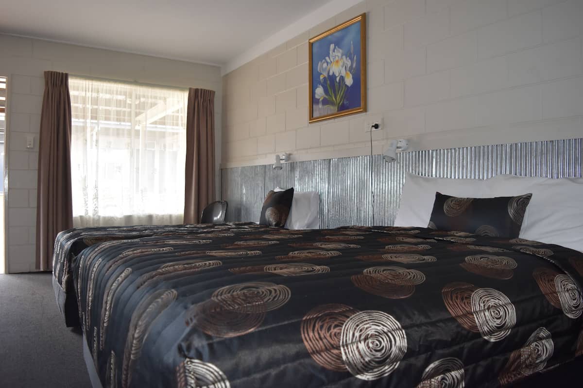 Ein Hotelzimmer mit einem großen Bett, einem Spiegel-Kopfschild, einem Bild an der Wand und einem Fenster mit Vorhängen.