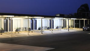 A hotel with a covered outdoor seating area, multiple rooms with large windows, and a parking lot. - Black Diamond Motel (Blackwater)