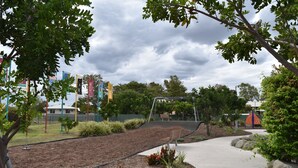 A landscaped area with a paved walkway, benches, and a playground structure. - Black Diamond Motel (Blackwater)