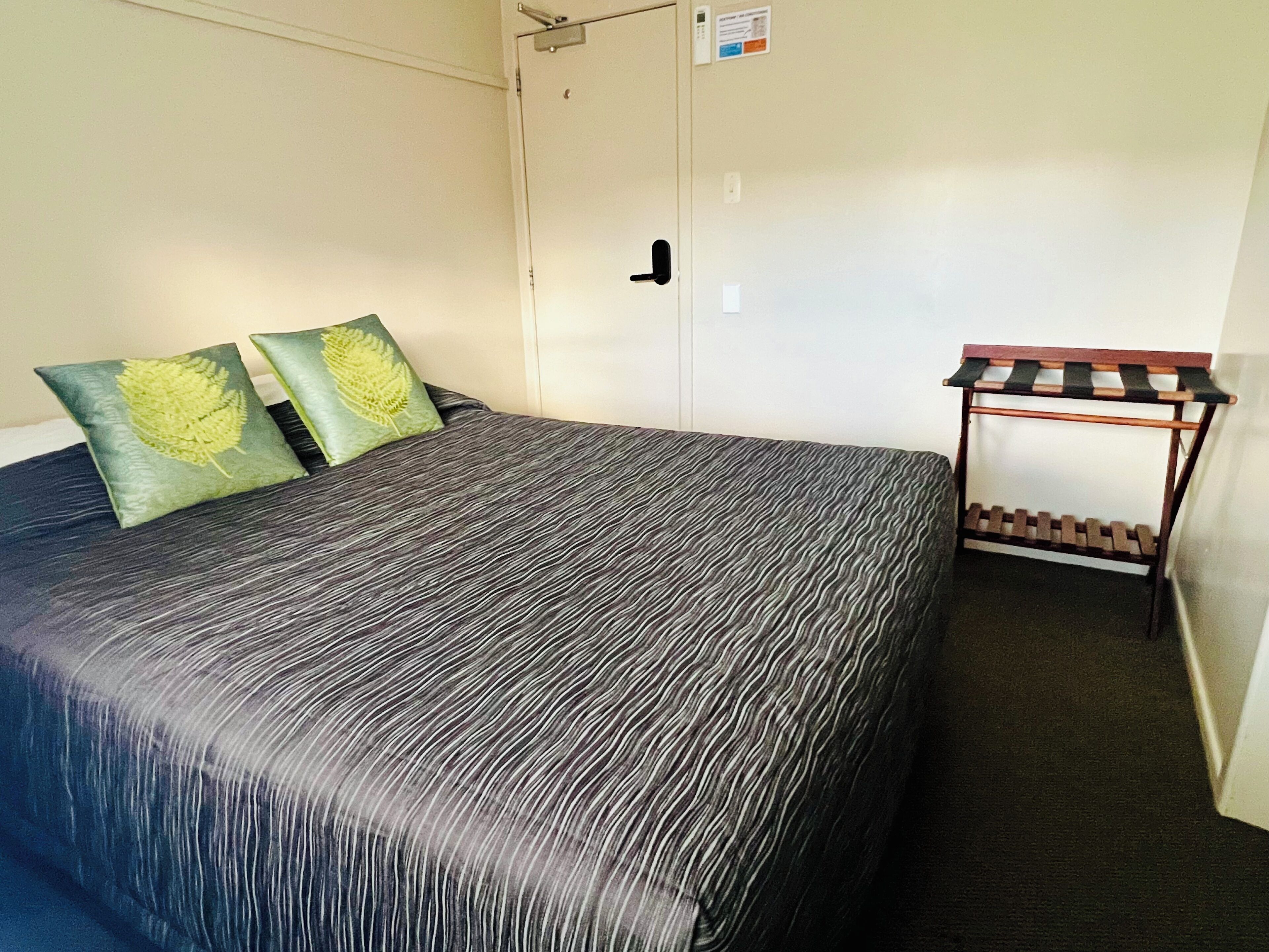 Una habitación con cama, dos almohadas, un banco de madera y una puerta.