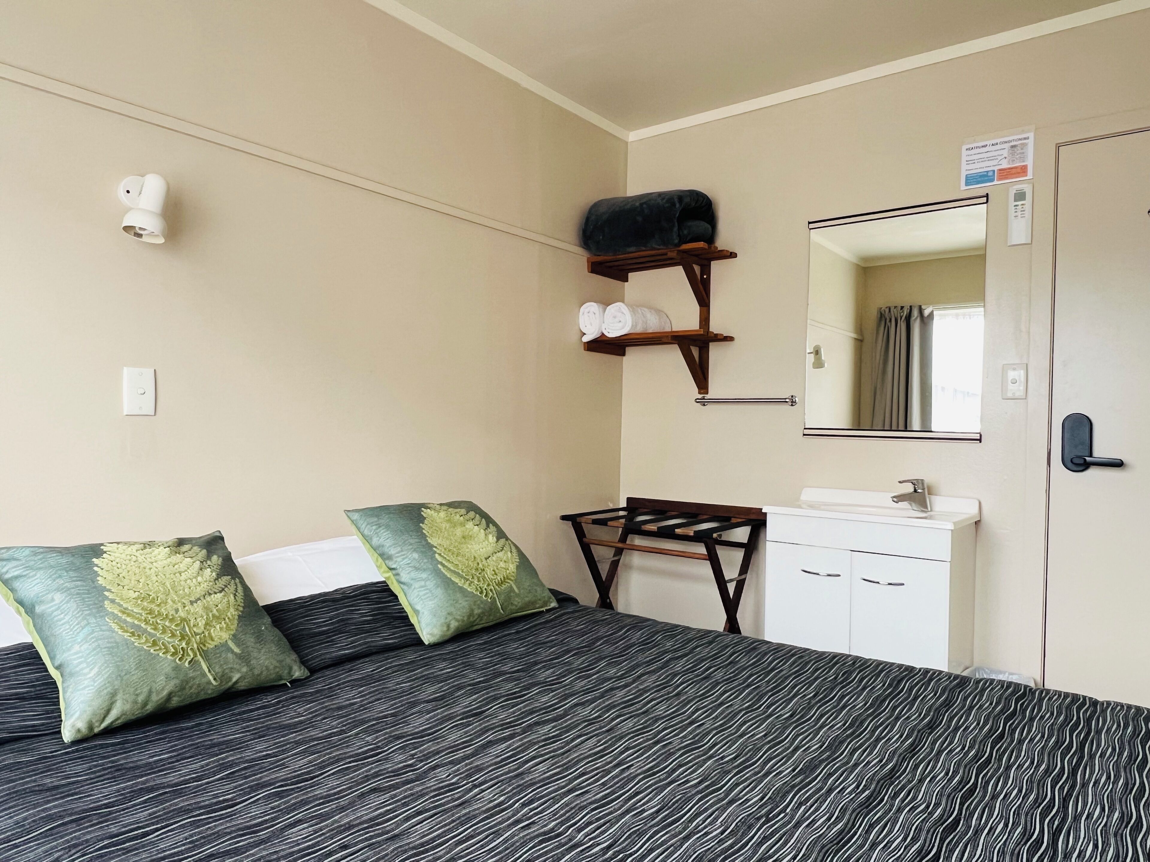 Ein Hotelzimmer mit einem Bett, einem kleinen Schreibtisch, einem Spiegel und einem Regal mit Handtüchern.