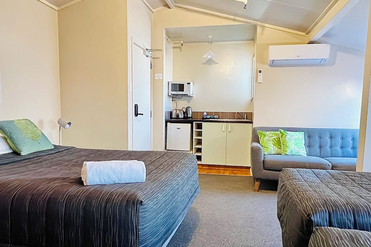 A room with two beds, a sofa, a kitchenette, and an air conditioning unit.