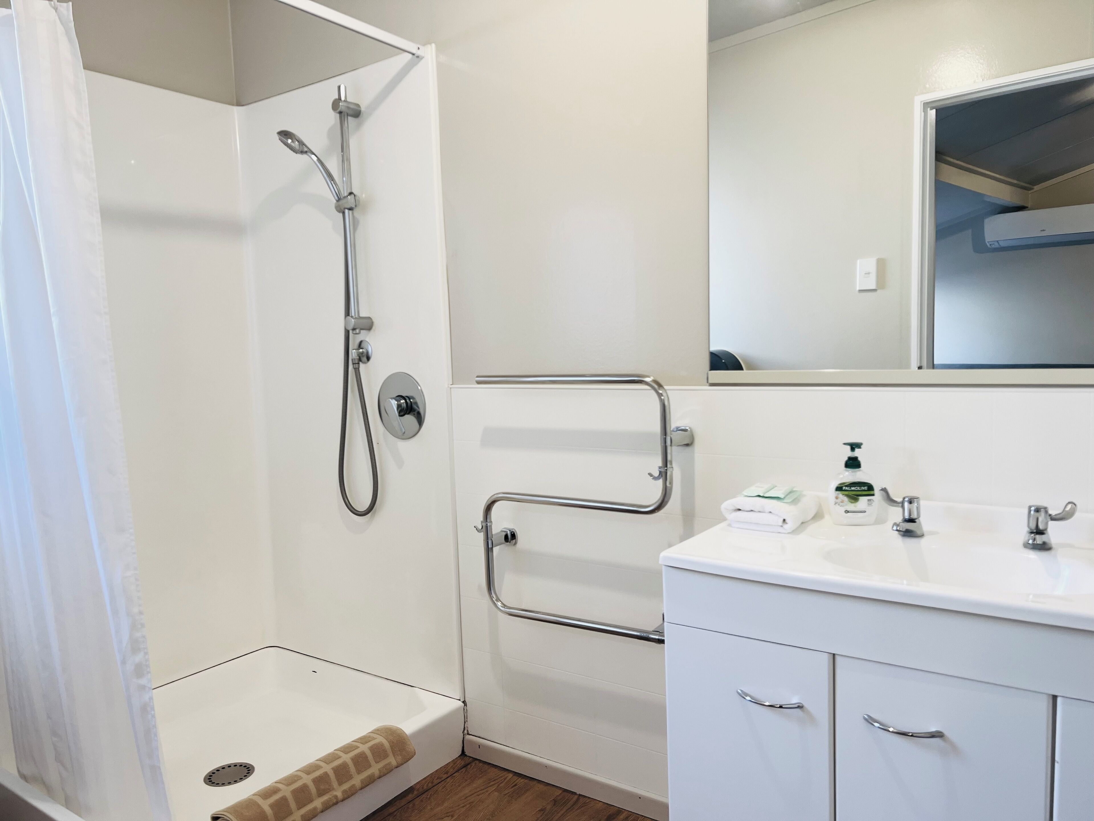 Un baño con ducha, inodoro, lavabo con espejo y dispensador de toallas.