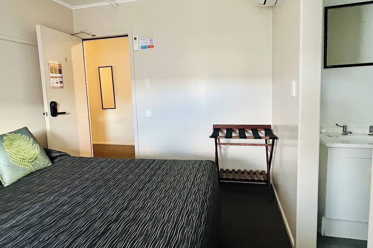 A hotel room with a bed, a bench, a sink, and a door leading to another room.