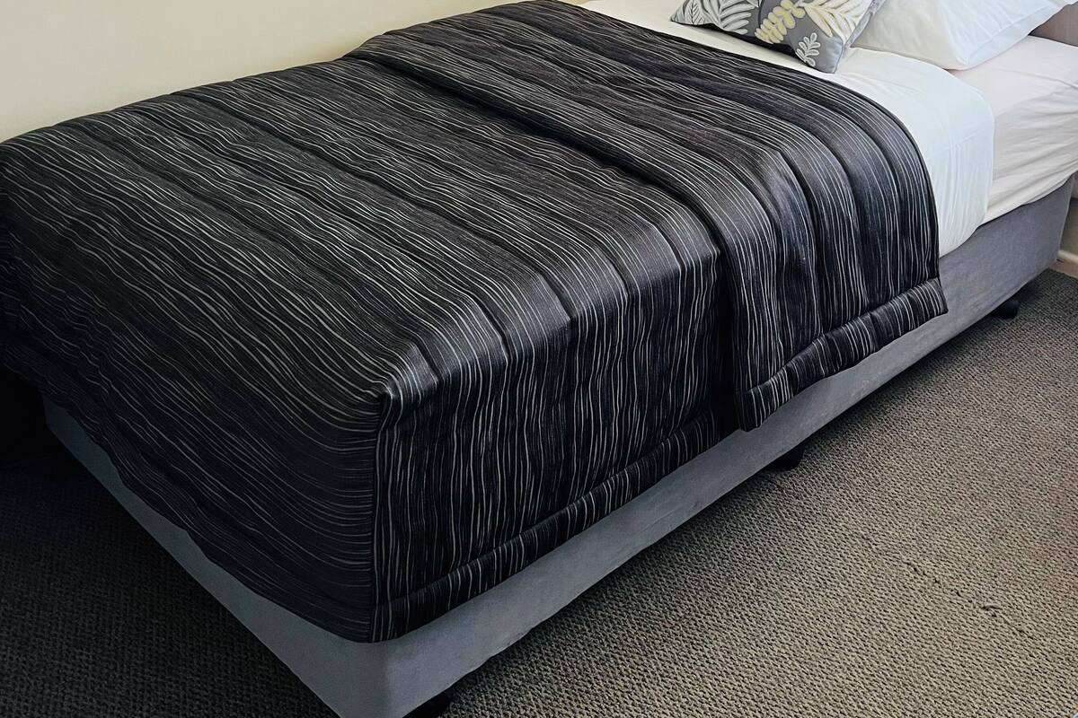 A neatly made bed with a black striped bedspread, a white pillow, and a floral pillow on a grey mattress.