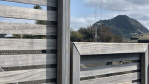 A wooden fence with a view of a mountain and some antennas in the background. - Seagulls Guesthouse (Tauranga)
