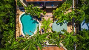 Oversigtsbillede af et resort med en swimmingpool omgivet af palmer og liggestole.