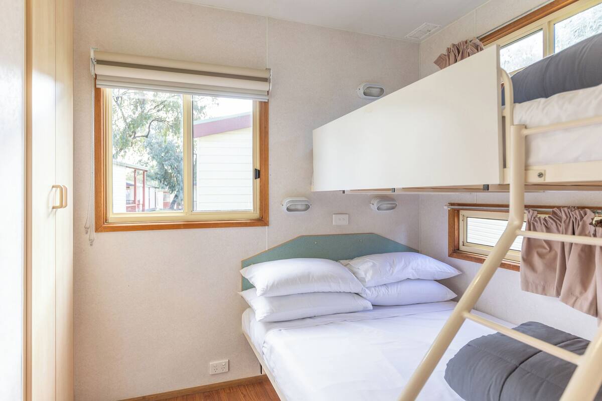Quarto com beliche, janela, porta e interruptor na parede.