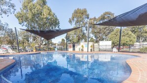 Ein Schwimmbecken mit einer gefliesten Kante, umgeben von einer Ziegelterrasse und beschattet durch eine große Markise.