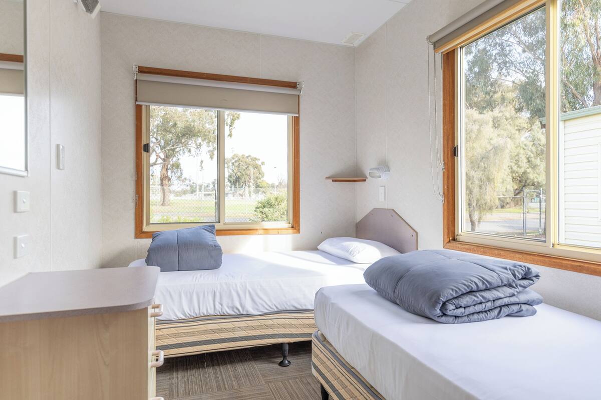Quarto com duas camas, uma escrivaninha e janelas amplas.