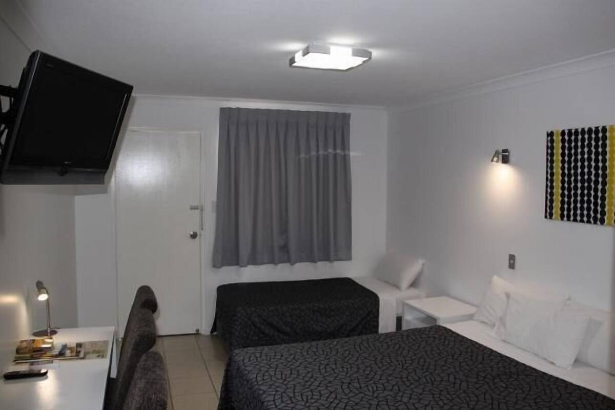 Habitación de hotel con cama, escritorio, silla, televisor montado en la pared y cortina.