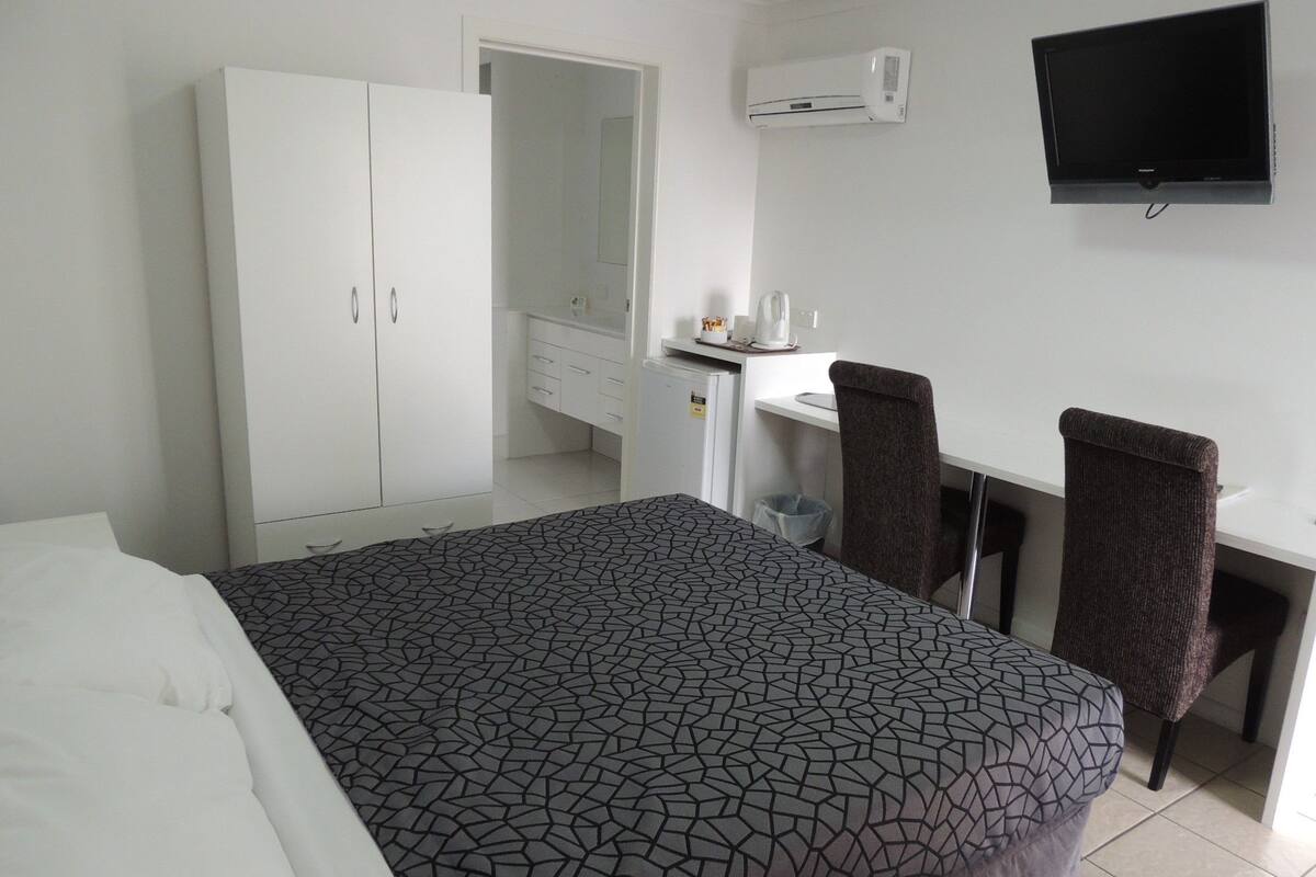 Una habitación de hotel con cama, escritorio, dos sillas, televisor y armario.