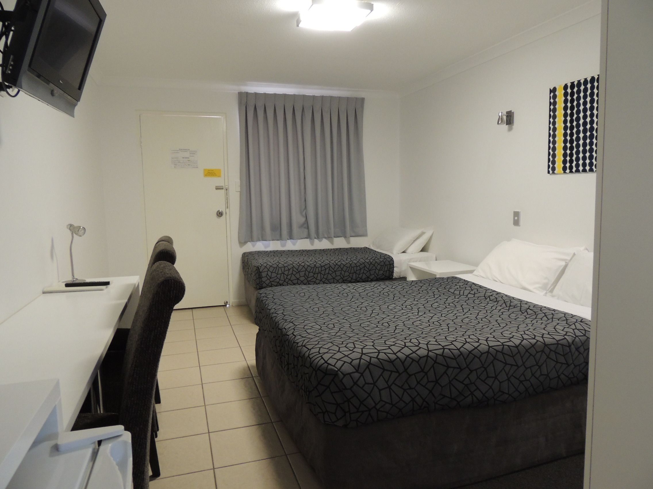 Habitación de hotel con dos camas, un escritorio, una silla, un televisor y una ventana con cortinas.