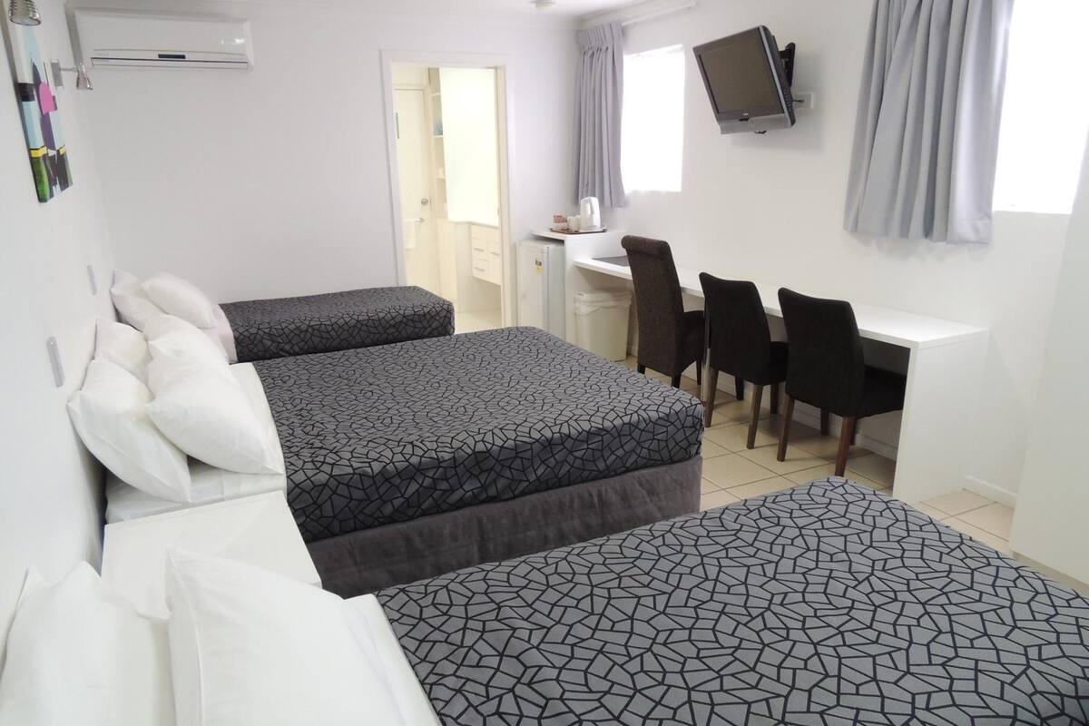 Habitación de hotel con dos camas, un escritorio, una silla, un televisor y un ventanal con cortinas.