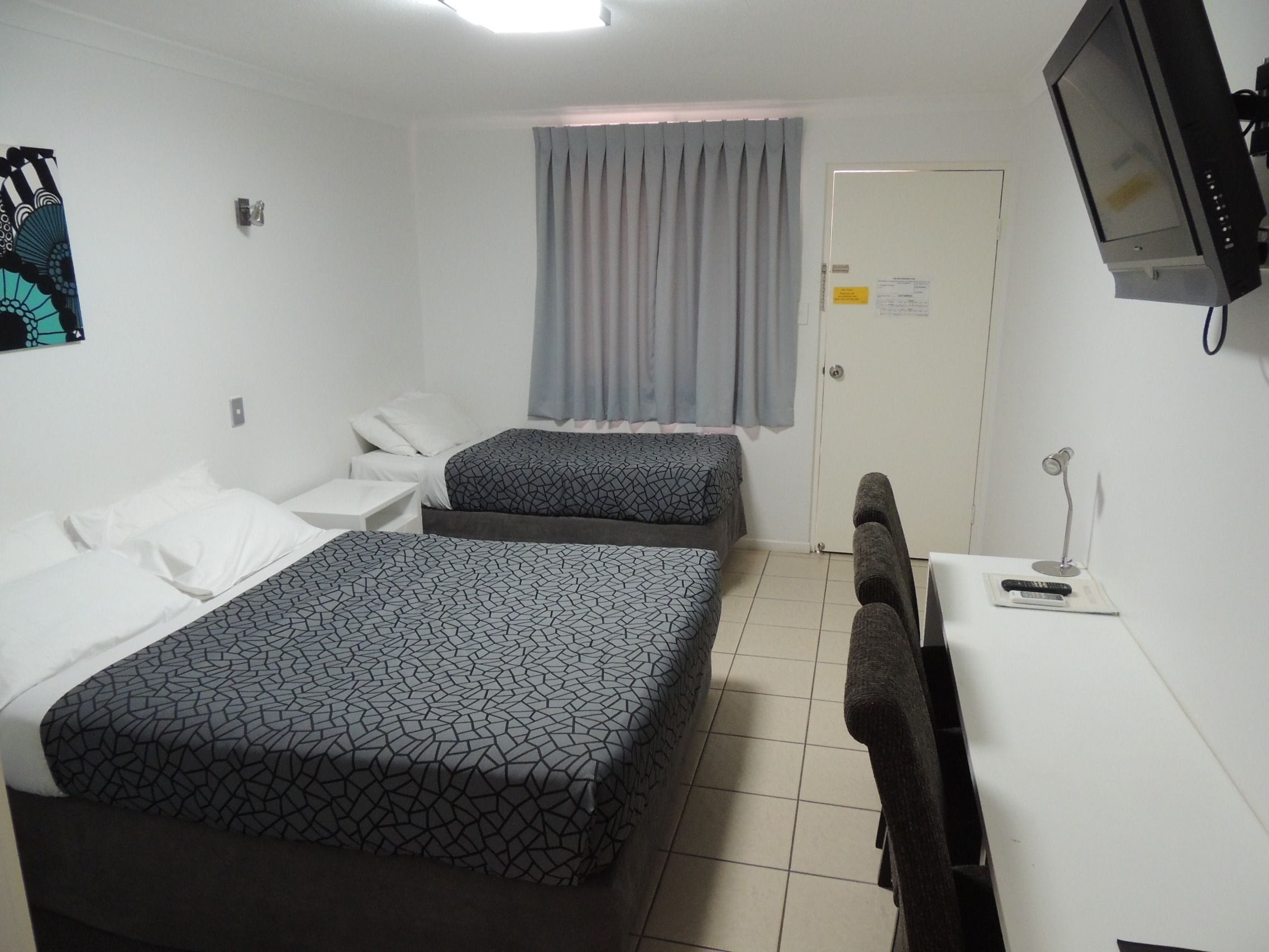 A hotel room with two beds, a desk, a chair, a TV, and a window with curtains.