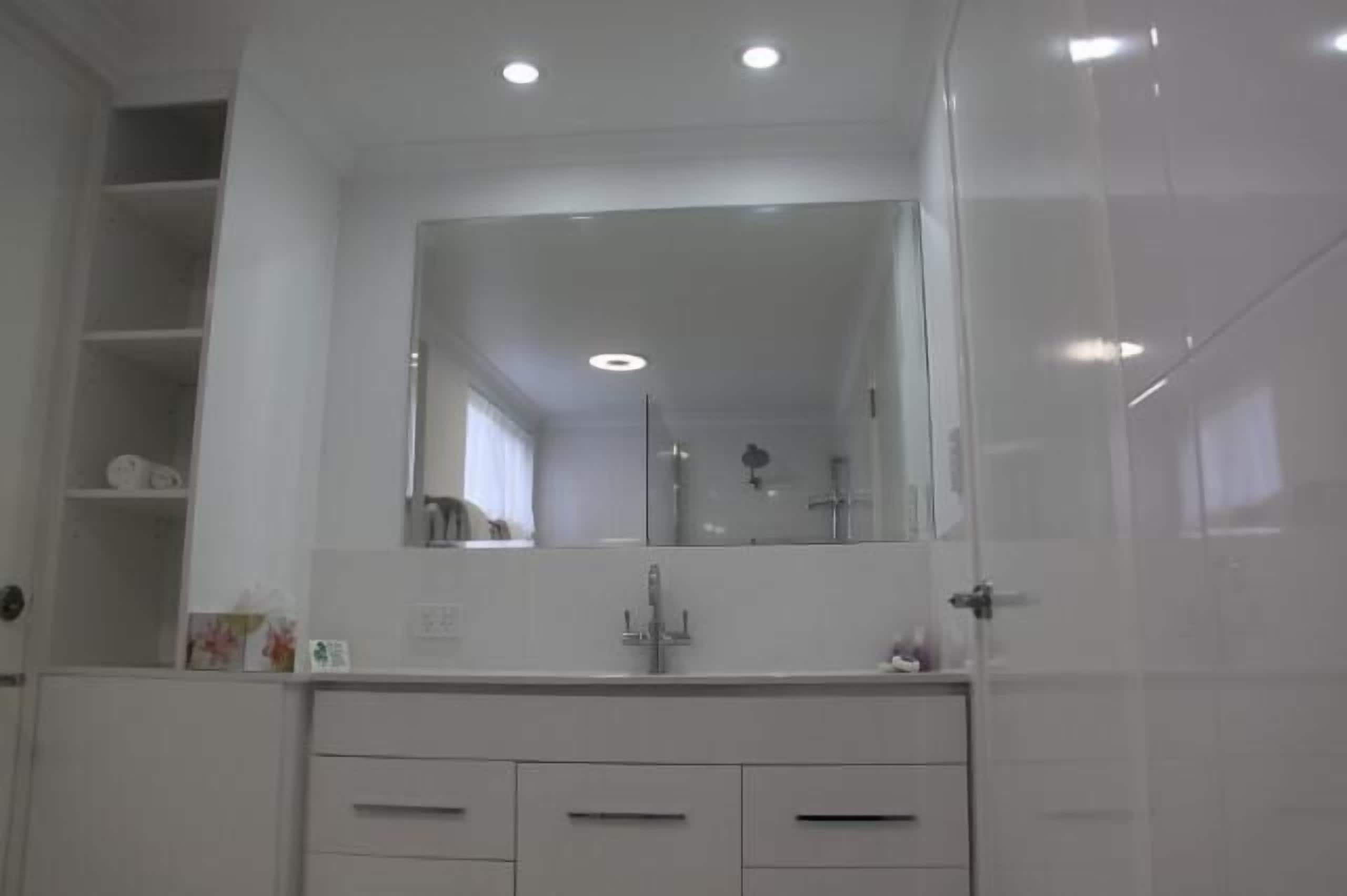 A bathroom with a large mirror, a sink, and a shower.