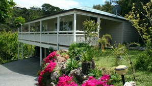A two-story house with a balcony, surrounded by a garden with pink flowers and various plants. - Villa Russell (Russell)