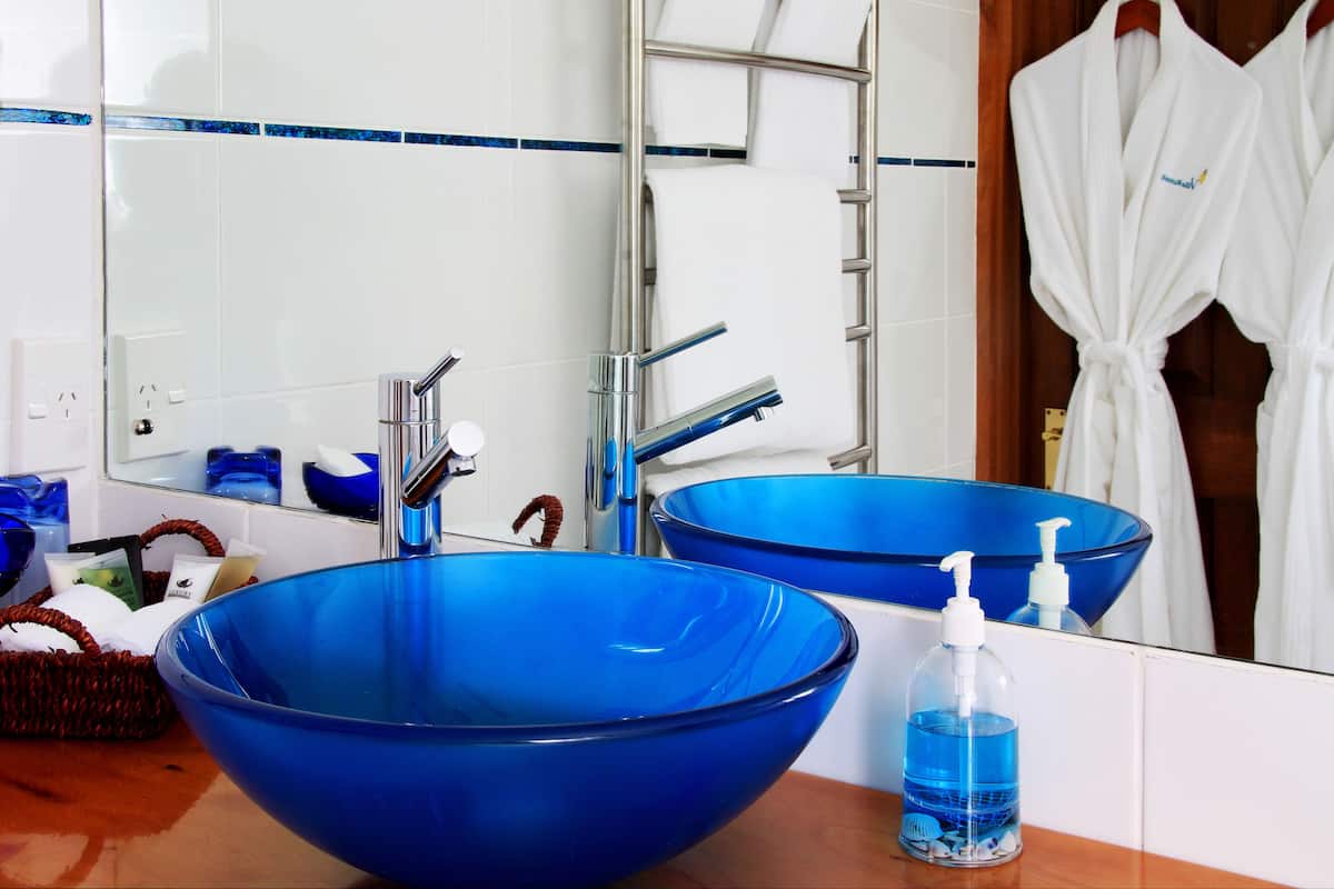 A bathroom with two large blue sinks, a chrome faucet, a mirror, and a rack with white robes.