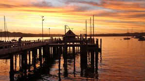 A pier extending into calm water with a small building at the end, surrounded by boats and a sunset sky. - Villa Russell (Russell)