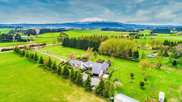 A large house with a garage, surrounded by green fields and trees, with a mountain in the background.
