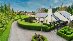 A house with a curved driveway, a patio with outdoor furniture, and a well-maintained garden. - Ruapehu Country Lodge (Ohakune)