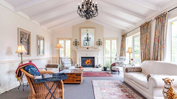 A spacious living room with a fireplace, a white sofa, a cheetah statue, and a large chandelier. - Ruapehu Country Lodge (Ohakune)