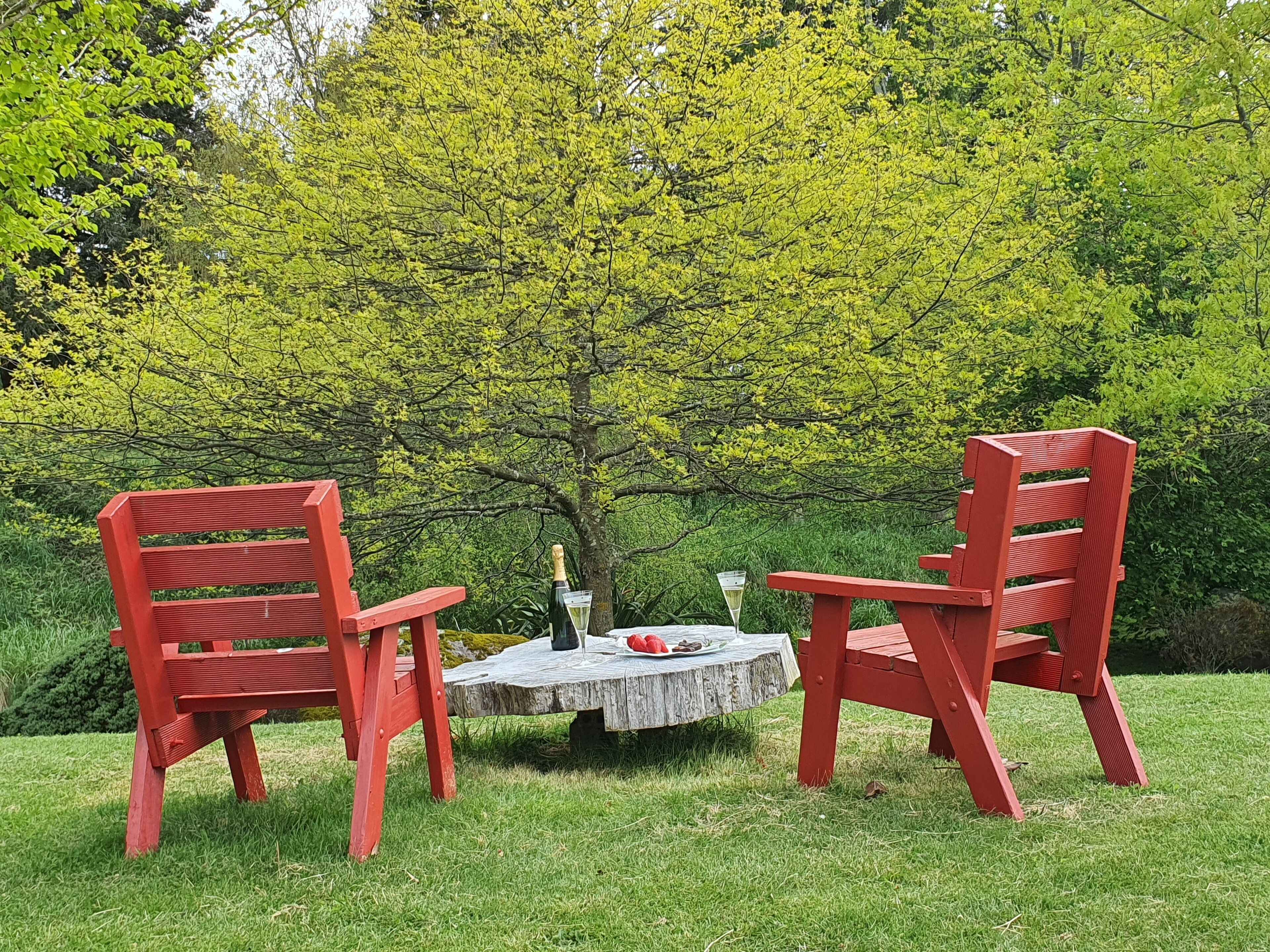 Due poltrone Adirondack rosse attorno a un piccolo tavolo di legno, con una bottiglia e un bicchiere.