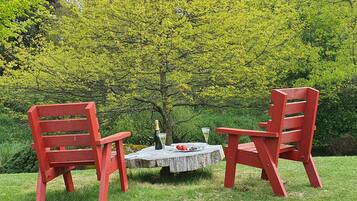 Duas cadeiras Adirondack vermelhas ao redor de uma pequena mesa de madeira, com uma garrafa e um copo.