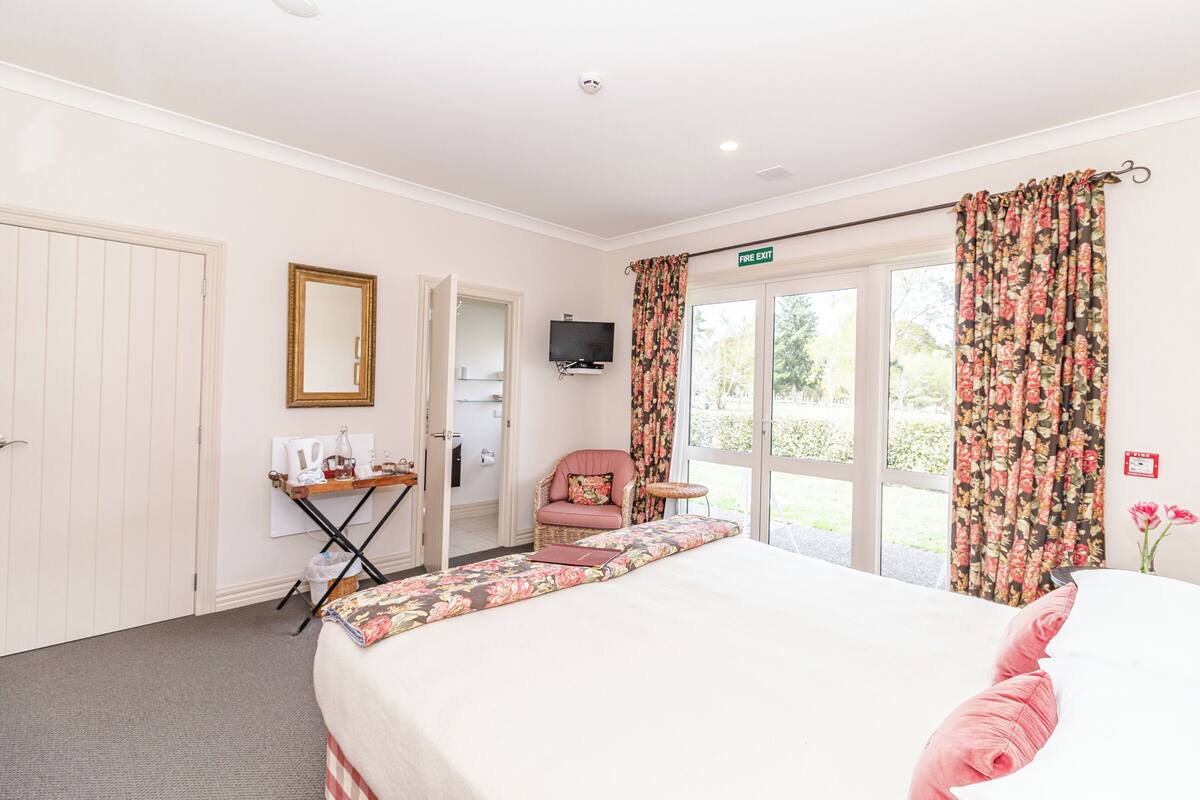 A hotel room with a bed, a chair, a small table, a television, and a view of the outdoors.