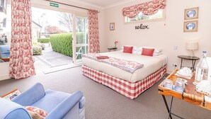 A bedroom with a bed, a blue sofa, a wooden side table, and a view of the outside. - Ruapehu Country Lodge (Ohakune)
