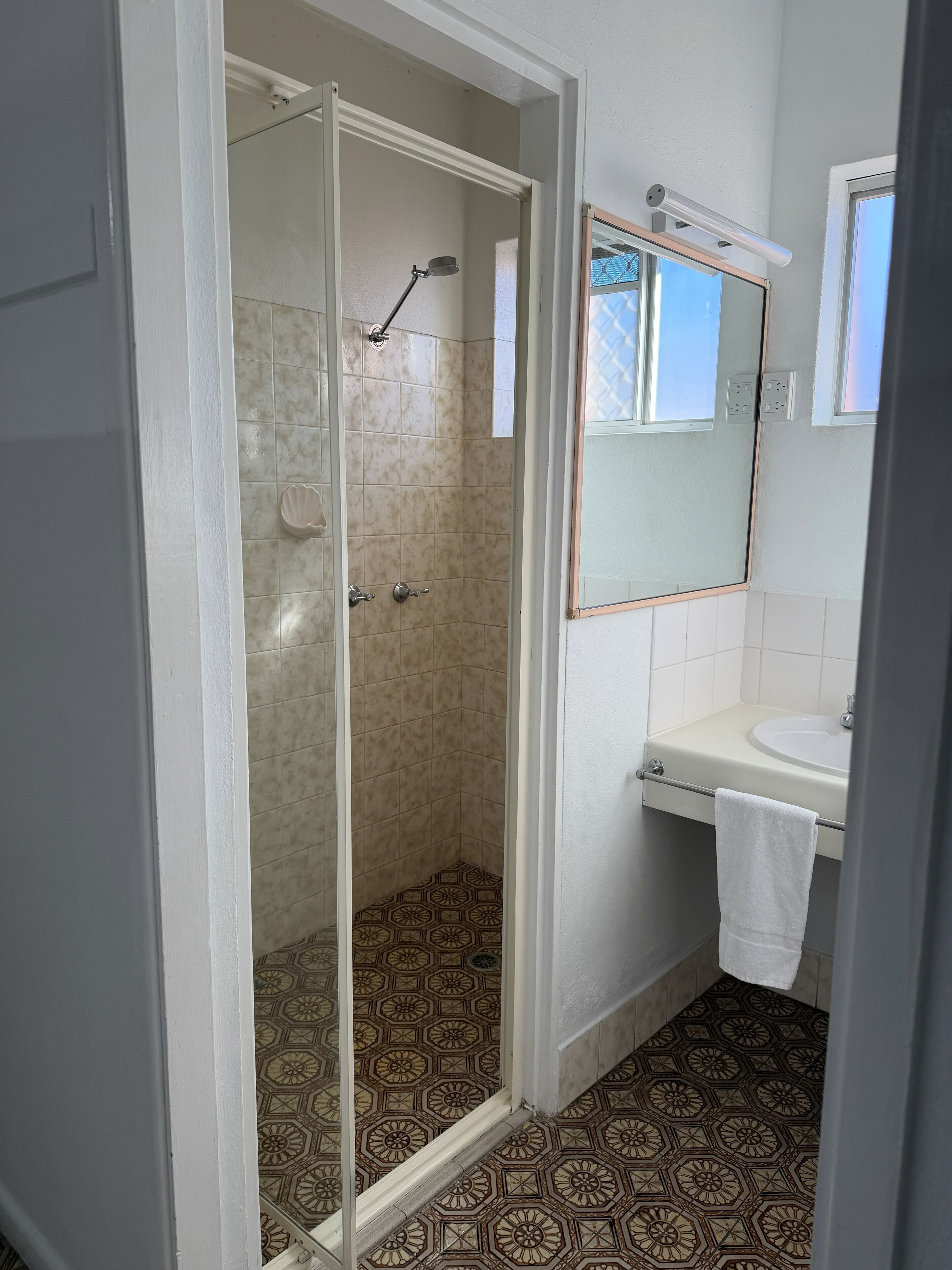 Ein Badezimmer mit Duschkabine aus Glas, einem Waschbecken mit Handtuch und einem Spiegel.